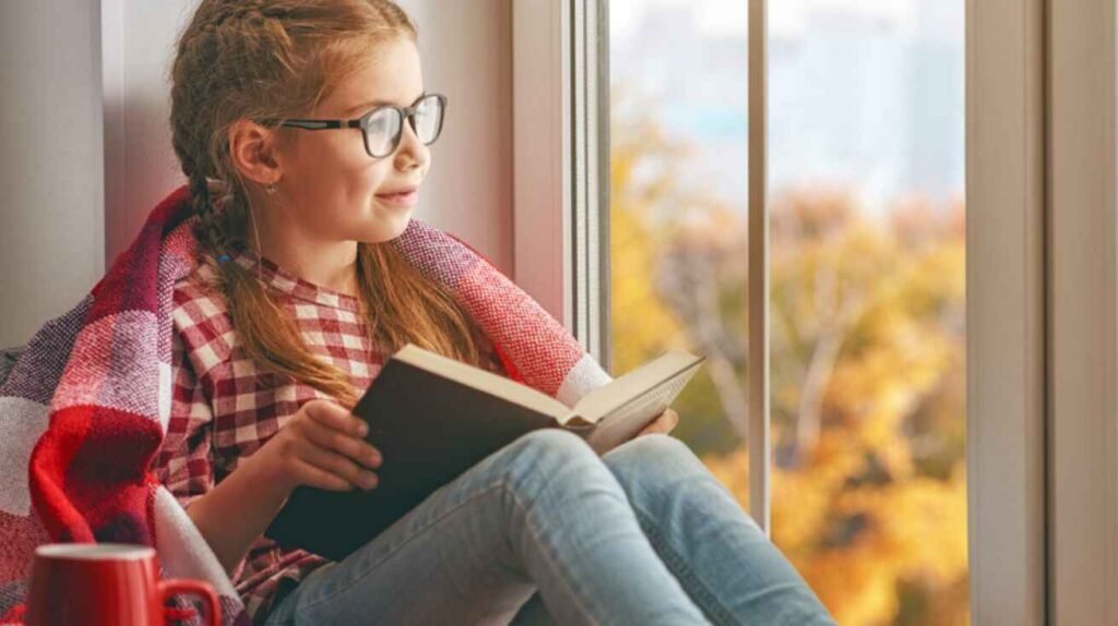 Student reading a book by the window, symbolizing how reading builds understanding and critical thinking.